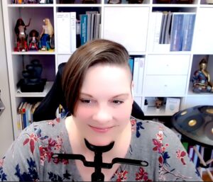 An older white woman in a gray shirt with flowers, short brown undercut hair, smiling with her chin leaning on an eye exam chin rest.